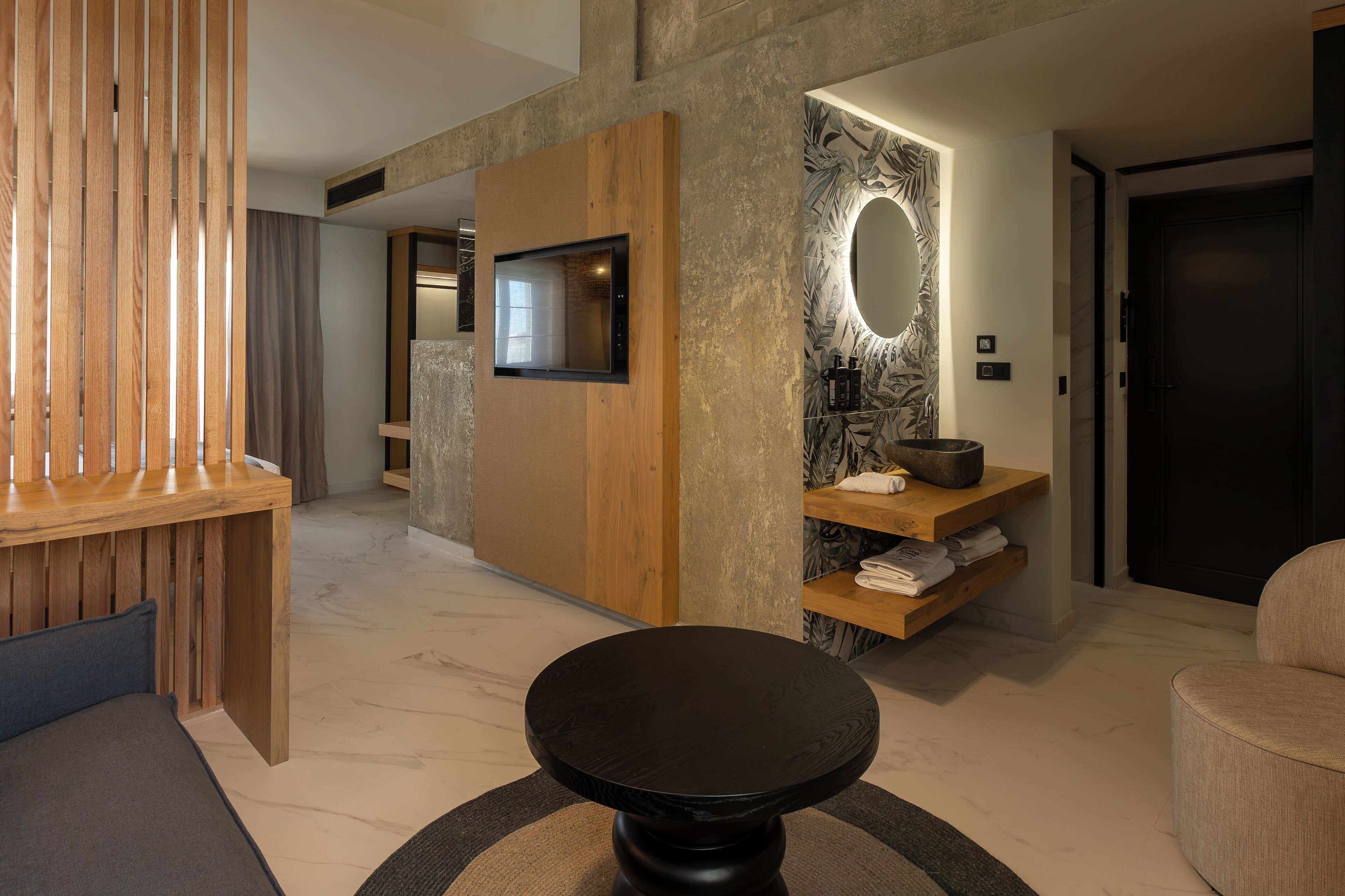 A modern hotel lobby with a wooden reception desk, a round black table, and a wall-mounted TV.