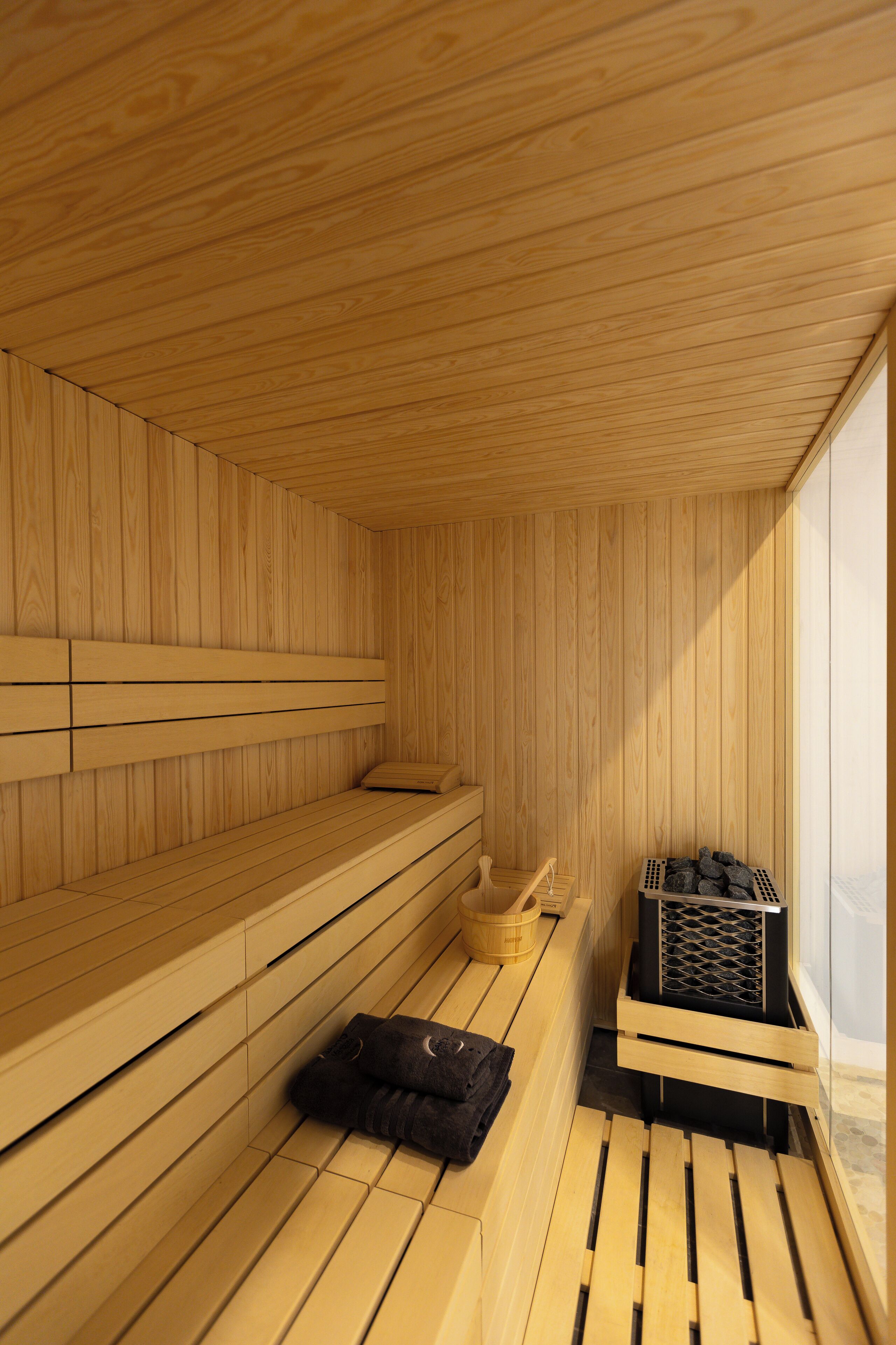 Una sauna de madera con bancos y un asiento de banco, piso de madera y una ventana.