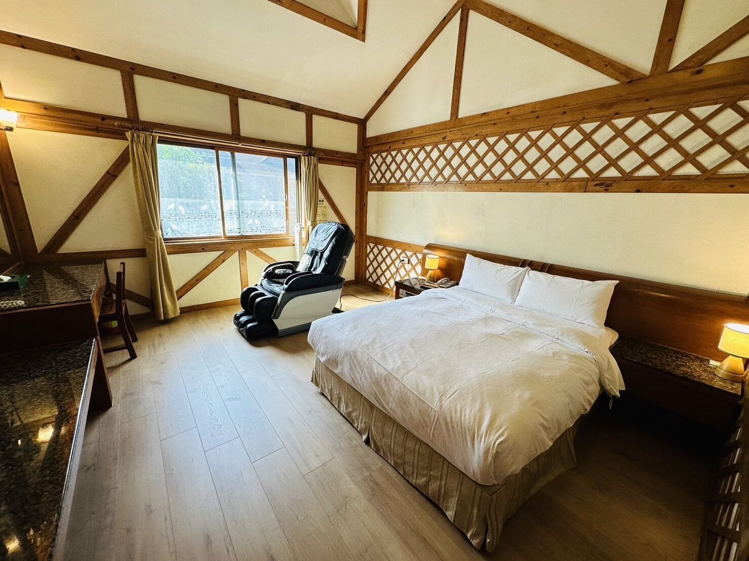 Un dormitorio con una cama grande, una silla de masaje, un escritorio y una ventana con cortinas.