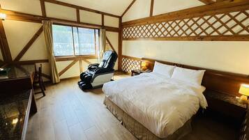Un dormitorio con una cama grande, una silla de masaje, un escritorio y una ventana con cortinas.
