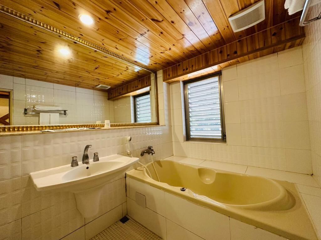 A bathroom with a wooden ceiling, a sink, a bathtub, and a window with blinds.