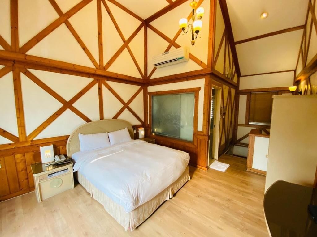 A bedroom with a large bed, wooden beams on the ceiling, a nightstand, and a chair.