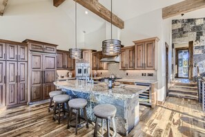 A spacious kitchen with wooden cabinets, a large island with stools, and hanging pendant lights.