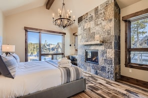 A bedroom with a large bed, a stone fireplace, and a view of a mountain.