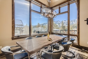 A dining area with a large table, chairs, a chandelier, and a mountain view.
