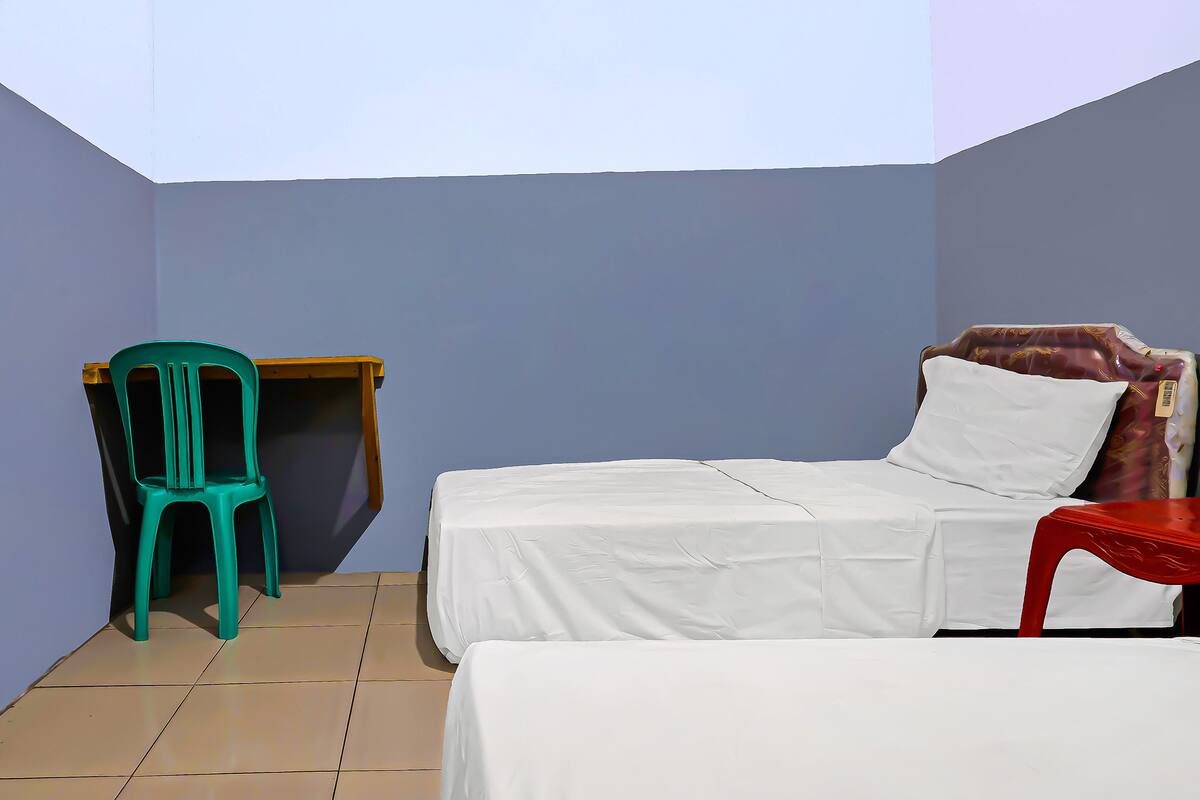 A small, single-bed room with a desk and chair, a tiled floor, and a plain wall.