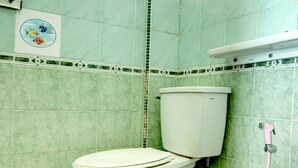 Een badkamer met toilet, groene betegelde wanden en een douchegedeelte.
