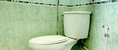 A bathroom with a toilet, green tiled walls, and a shower area.