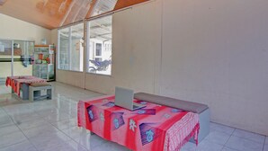 Een ruime kamer met een grote tafel, bedekt met een tafelkleed met een patroon, een laptop op de tafel en een bankje op de achtergrond.