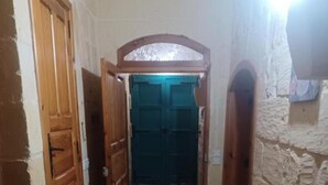 A narrow hallway with wooden doors on either side, leading to a room with a tiled floor and a window with frosted glass. - Peace Heaven Farmhouse Zebbug Gozo, With Pool (Zebbug)
