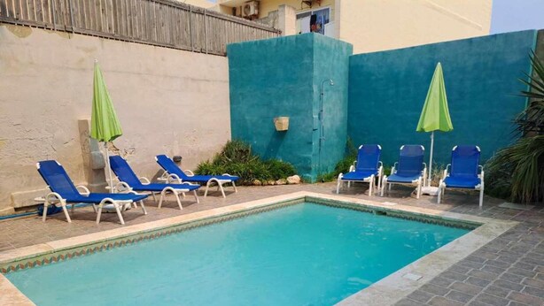 A swimming pool with blue water, surrounded by lounge chairs and umbrellas. - Peace Heaven Farmhouse Zebbug Gozo, With Pool (Zebbug)