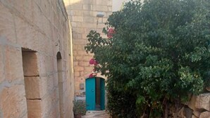 A narrow alleyway with a stone wall on one side and a building on the other. There is a blue door at the end of the alley. - Peace Heaven Farmhouse Zebbug Gozo, With Pool (Zebbug)