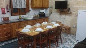 A rustic kitchen with wooden cabinets, a tiled floor, and a dining table set for six.