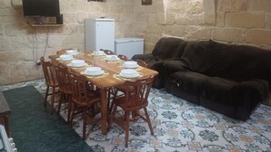 A dining area with a wooden table set for six, surrounded by chairs, a brown sofa, and a tiled floor. - Peace Heaven Farmhouse Zebbug Gozo, With Pool (Zebbug)