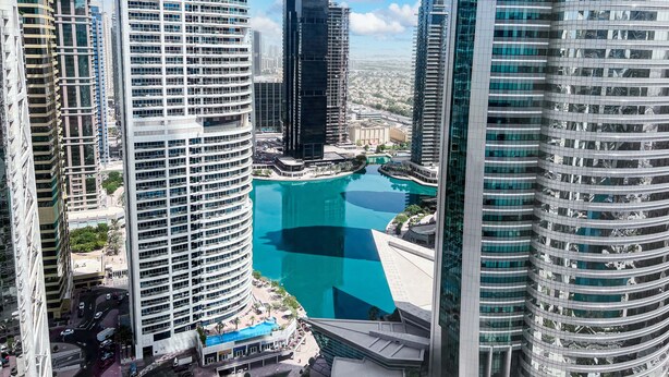 Un immeuble de grande hauteur à la façade incurvée, doté d’une cour intérieure avec une piscine, et entouré d’autres immeubles modernes de grande hauteur.