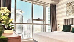 Une chambre d’hôtel moderne, dotée d’un grand lit, d’un bureau et offrant une vue sur le paysage urbain grâce à de grandes fenêtres.