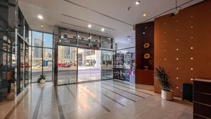 Rebost d'hotel modern amb portes de vidre que donen a la vista d'un carrer, una taula de recepció i una planta en test.