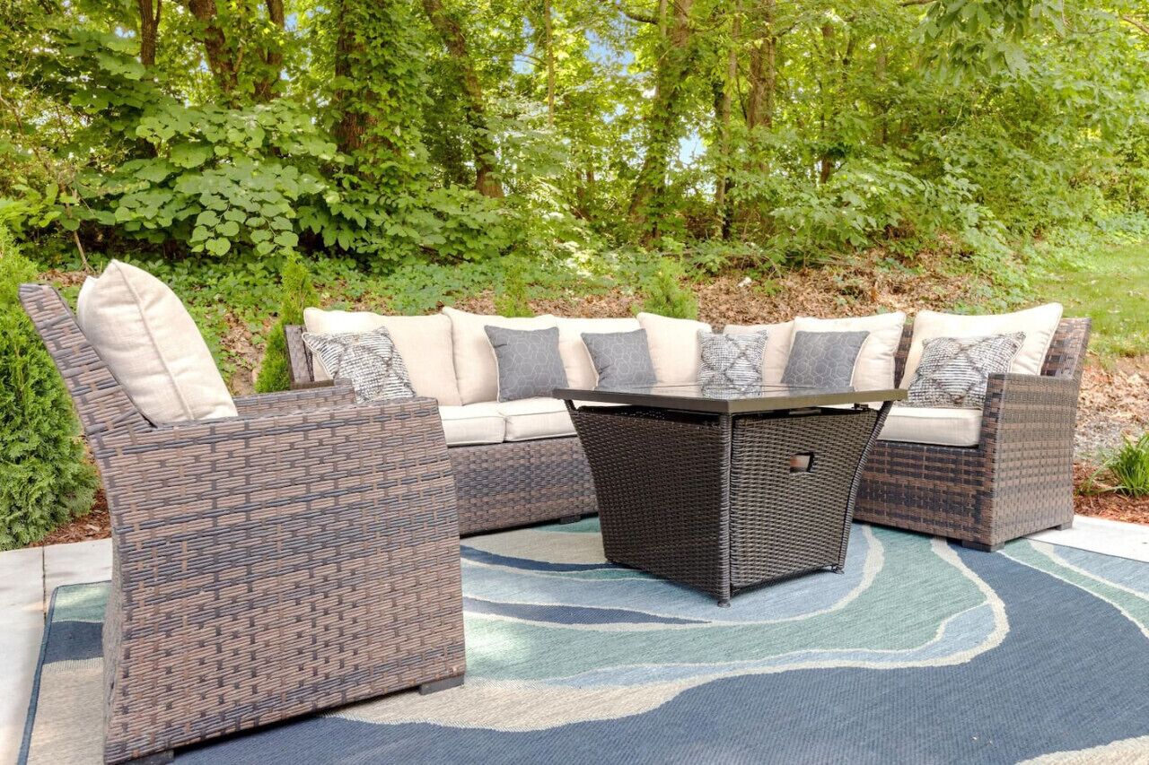 A sectional outdoor sofa with a woven design and cushioned seats, a matching coffee table, and a patterned rug on a patio.