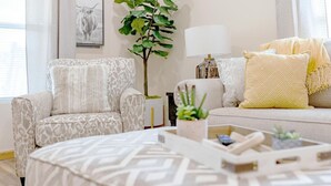 A living room with a patterned sofa, a side table with a lamp, a potted plant, and a decorative tray.