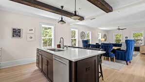 A spacious kitchen with a large island, wooden beams, and a dining area with blue chairs.
