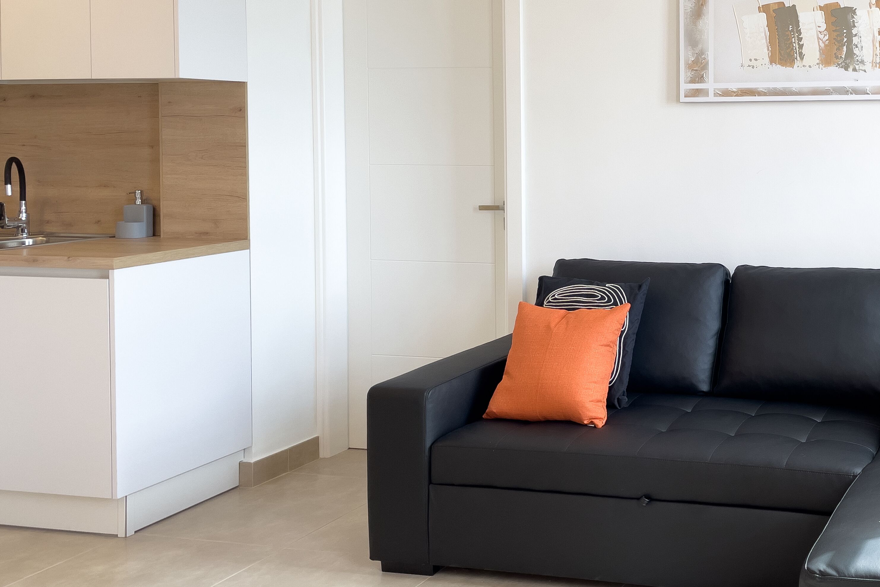 A modern kitchen with a wooden countertop and a black leather sofa with an orange pillow.