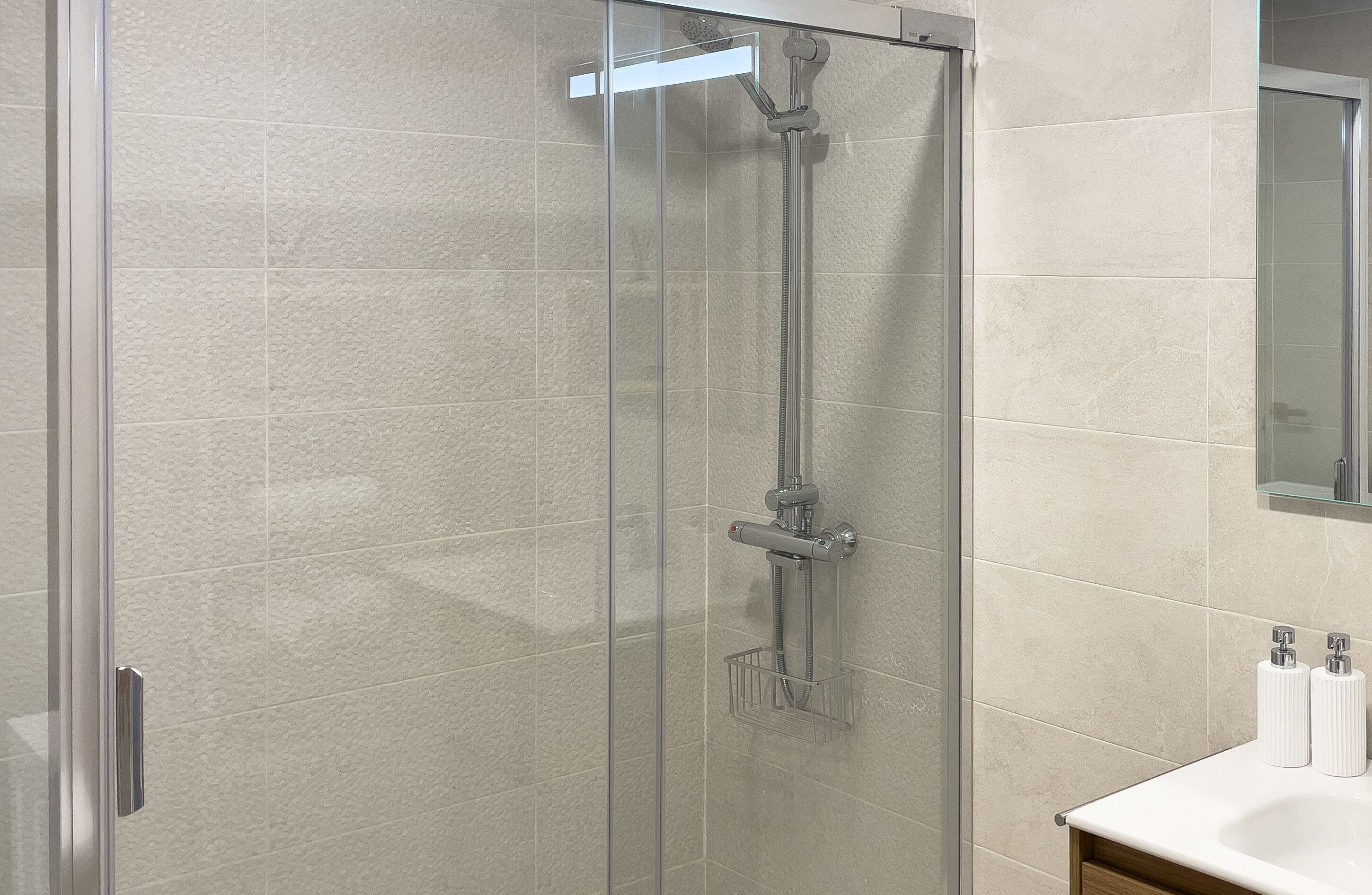 A modern bathroom with a glass-enclosed shower, a white sink, and a mirror above the sink.