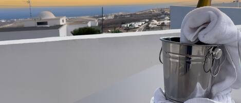 Un seau en métal, une bouteille de champagne, une serviette blanche et une assiette, le tout posé sur un balcon donnant sur un paysage urbain le long de la côte.