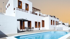 Un edificio blanco con piscina, puertas de madera y zona de estar al aire libre.