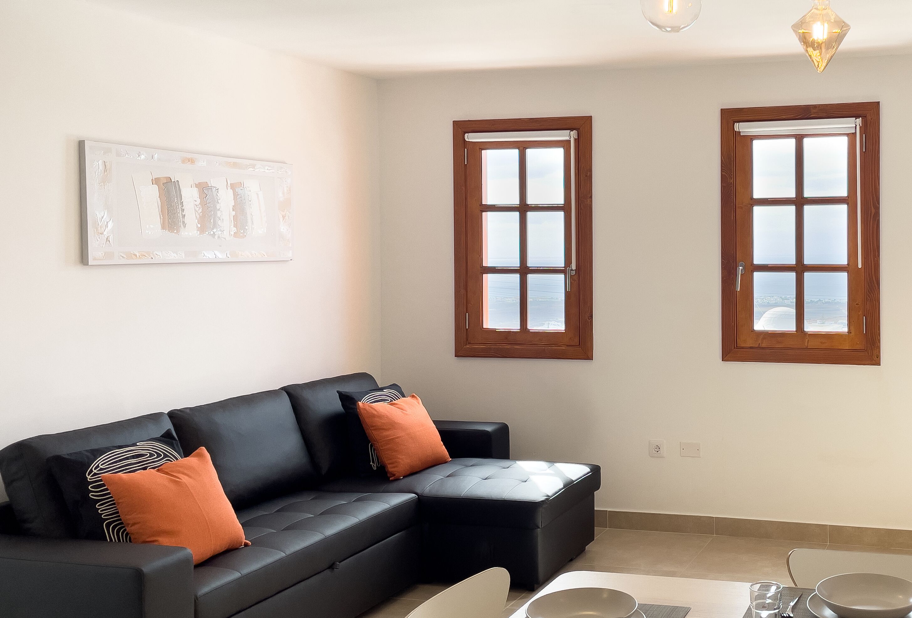 A modern living room with a black sectional sofa, two windows, and a painting on the wall.