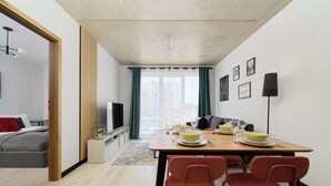 Un salon moderne comprenant un coin repas, un canapé, un téléviseur et une grande fenêtre agrémentée de rideaux.