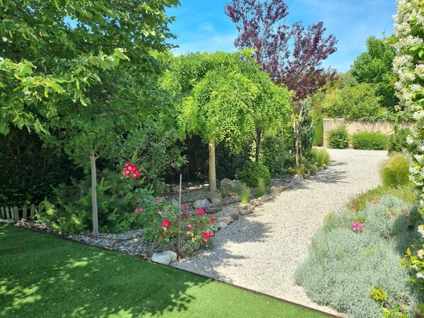 A garden with a gravel path, green grass, and various plants and flowers.