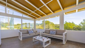 A sunlit room with a wooden ceiling, large windows, and a sectional sofa with patterned cushions.