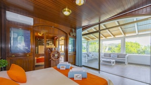 Een groot bed met oranje kussens, een houten plafond en uitzicht op een balkon met een bank.