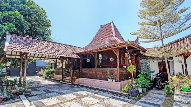 Ein traditioneller hölzerner Pavillon mit Ziegeldach, umgeben von Topfpflanzen und einem mit Steinplatten gepflasterten Innenhof.