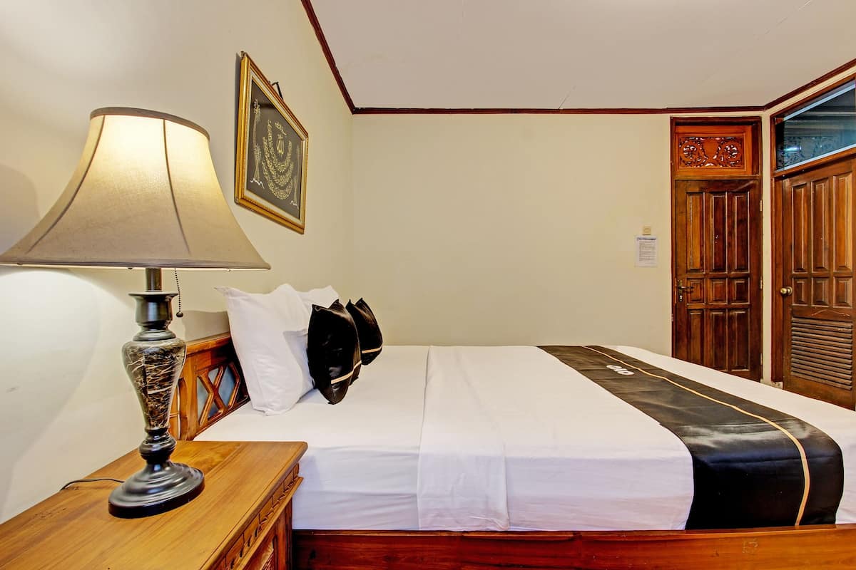 Une chambre d’hôtel avec un lit, une lampe, un tableau encadré et une porte en bois.