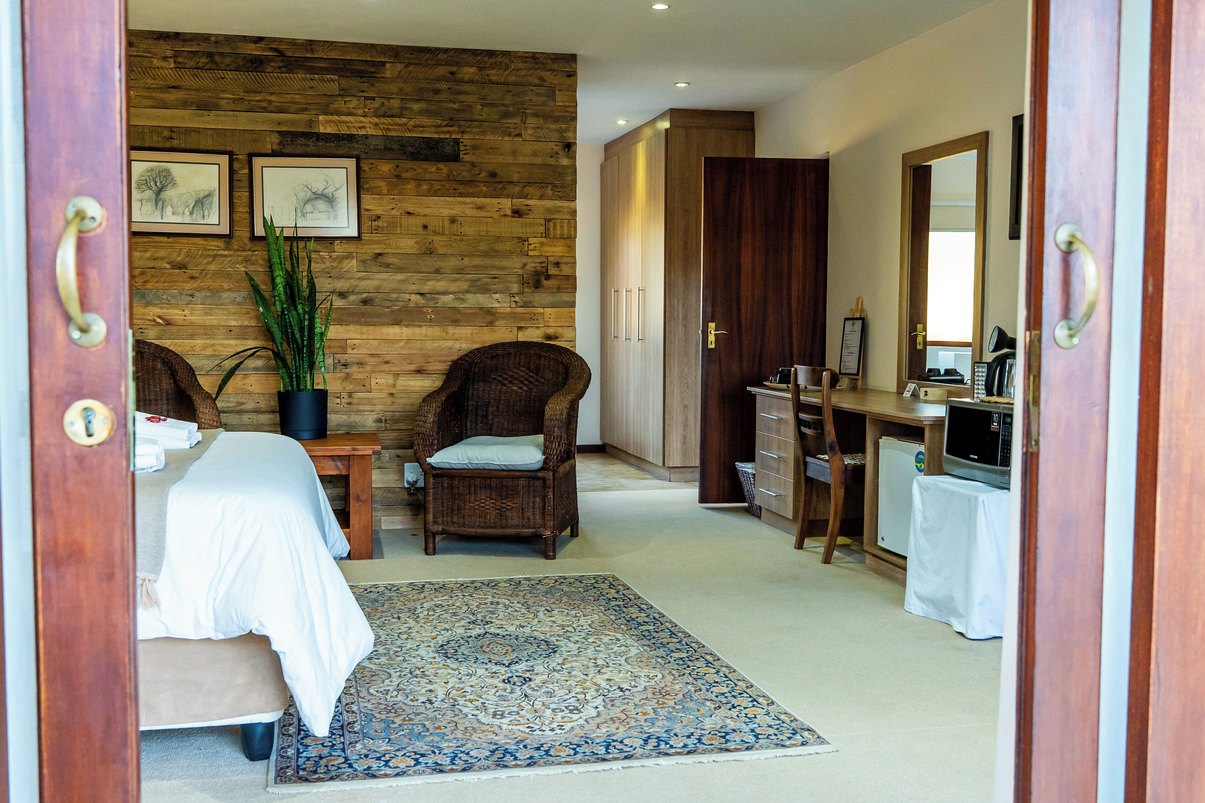 Um quarto com cama, cadeira, escrivaninha, cômoda, espelho e planta em vaso.