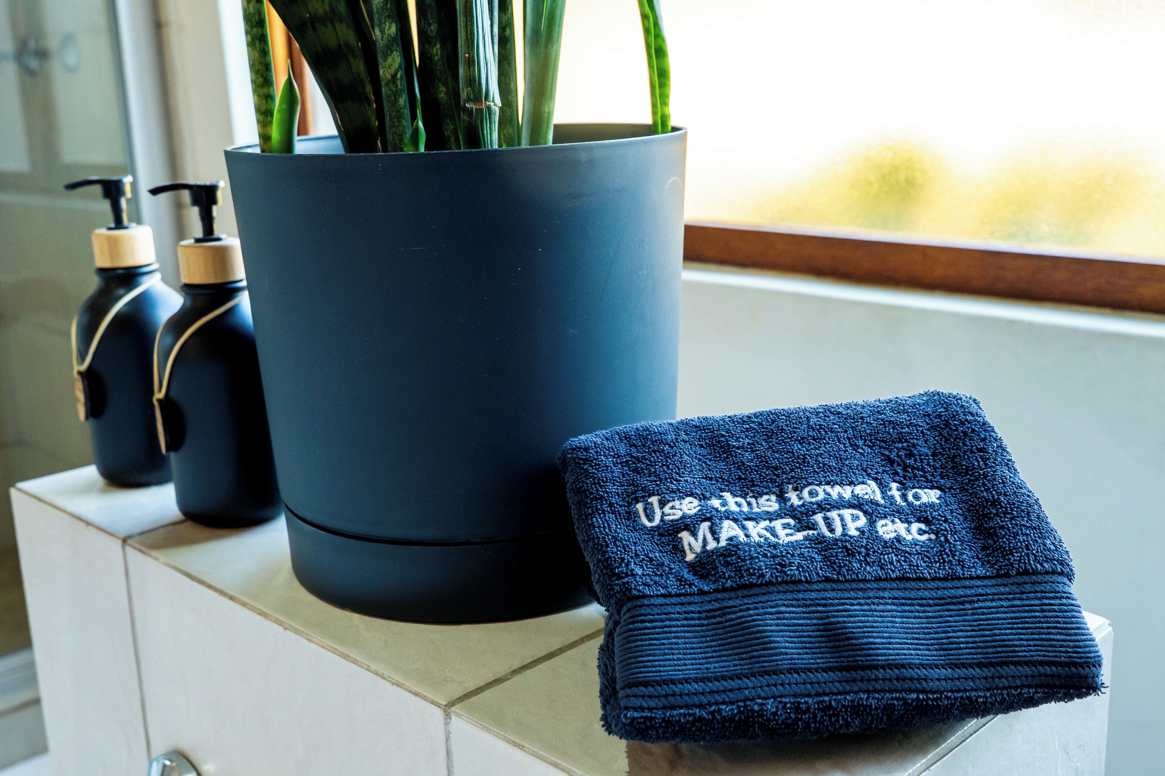 A bathroom with a potted plant, two bottles of lotion, and a folded towel with text.