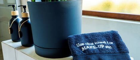 A bathroom with a potted plant, two bottles of lotion, and a folded towel with text.