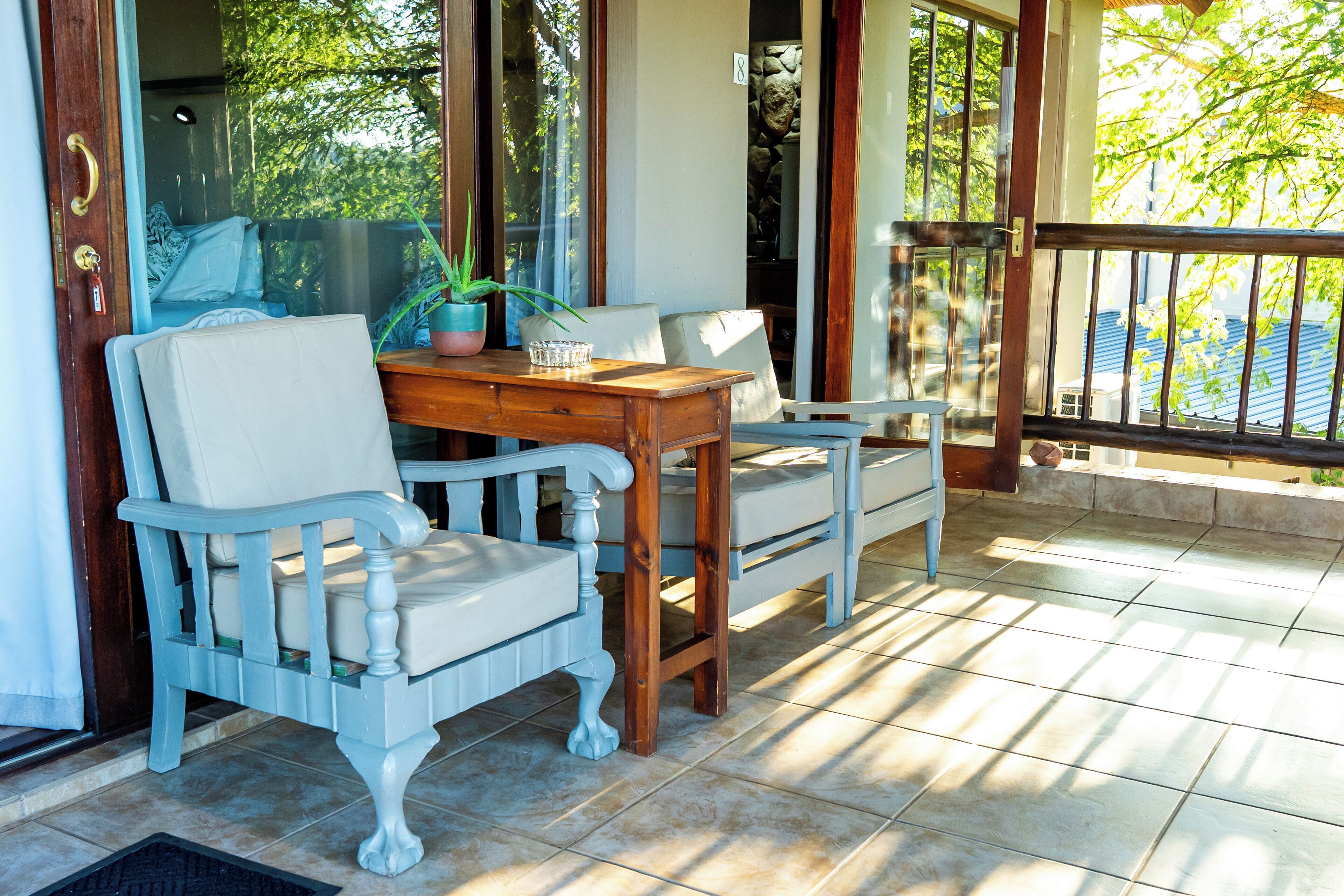 A wooden table and two white chairs with cushioned seats, positioned on a tiled floor.