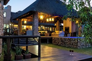 A resort with a thatched-roof lounge area, stone walls, and a wooden deck.