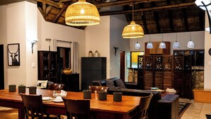 Ampla sala de estar com mesa de jantar de madeira, assentos confortáveis e luminárias modernas.