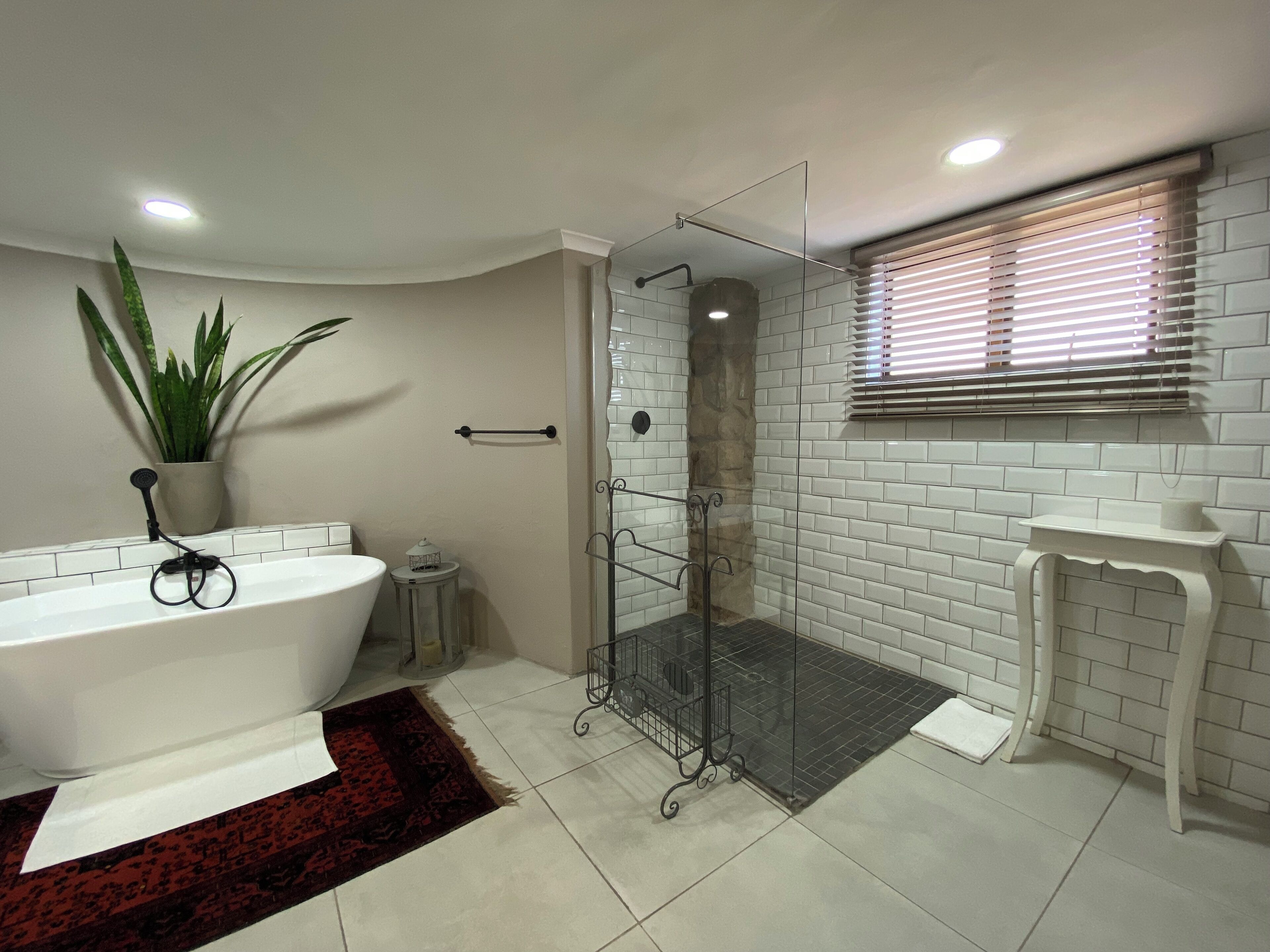 A modern bathroom with a freestanding bathtub, a glass-enclosed shower, and a white tiled wall.