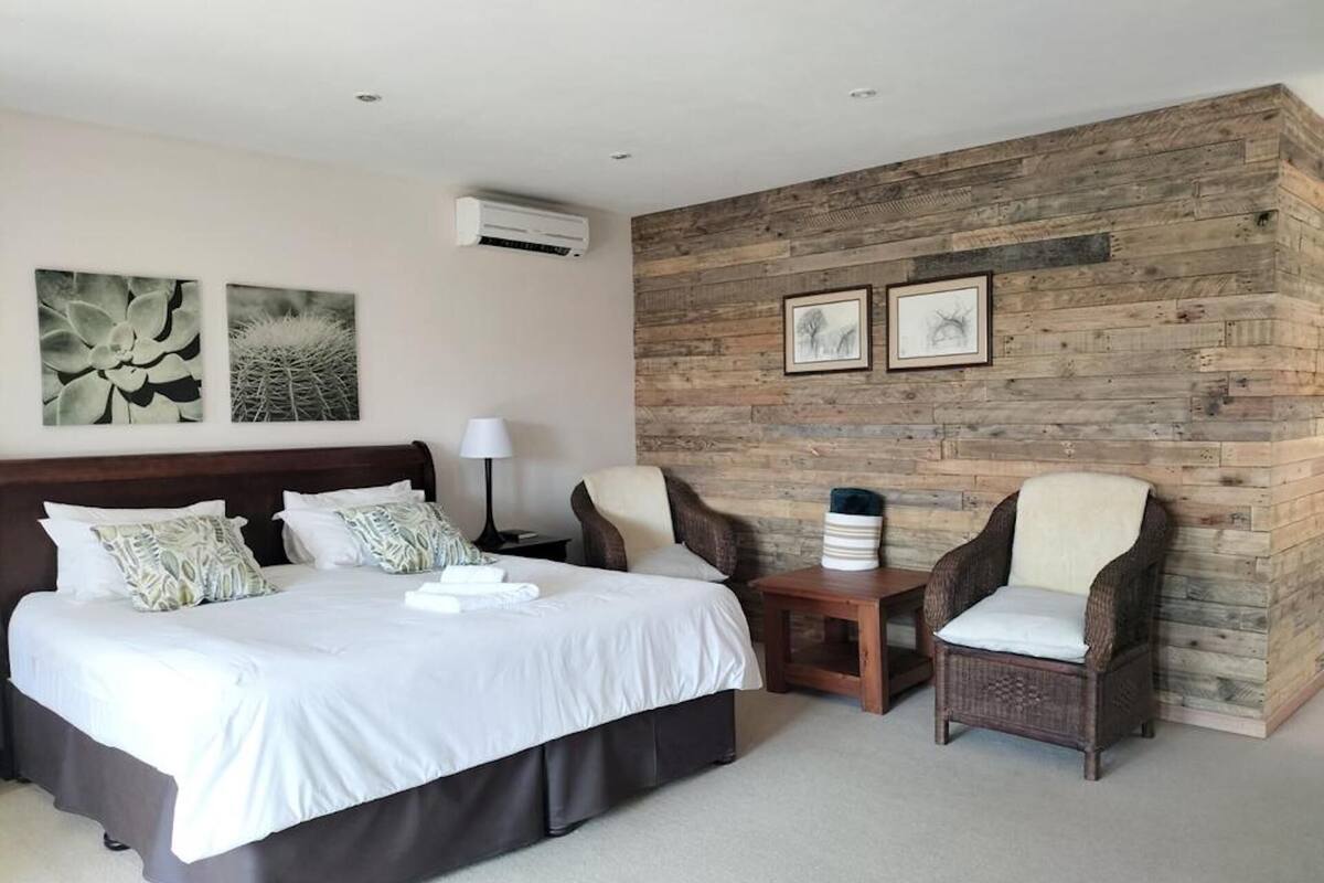 A hotel room with a large bed, two armchairs, a small table, and artwork on the walls.