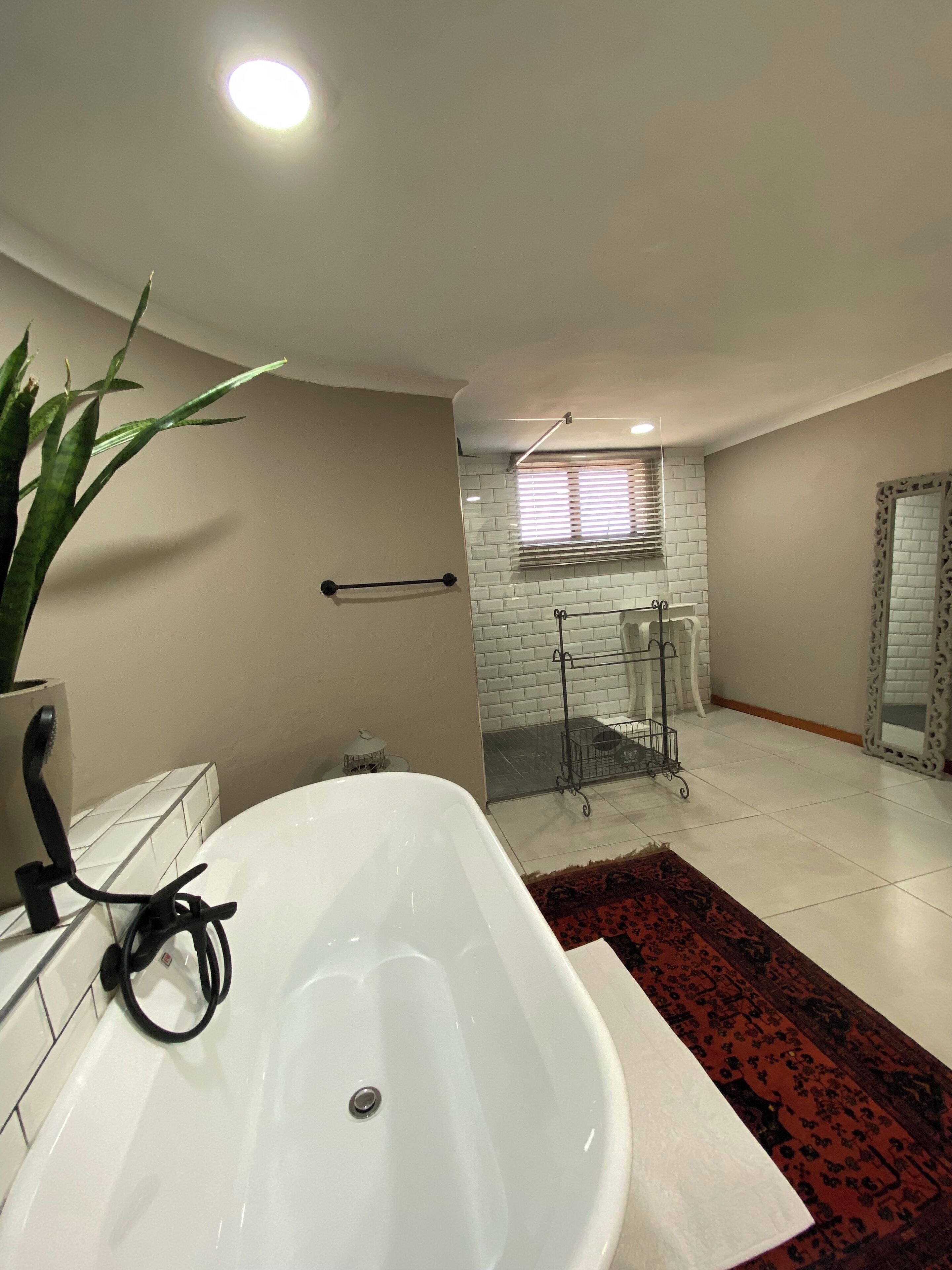 Een moderne badkamer met een vrijstaand bad, een potplant, een handdoekrek en een raam met zonwering.