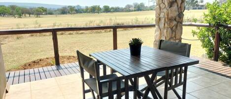 Eine Terrasse im Freien mit Tisch und Stühlen, einer Stein Säule und Blick auf ein grünes Feld.