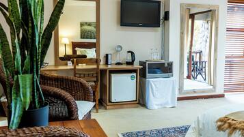 A hotel room with wicker furniture, a small refrigerator, a television, and a view of the outside.