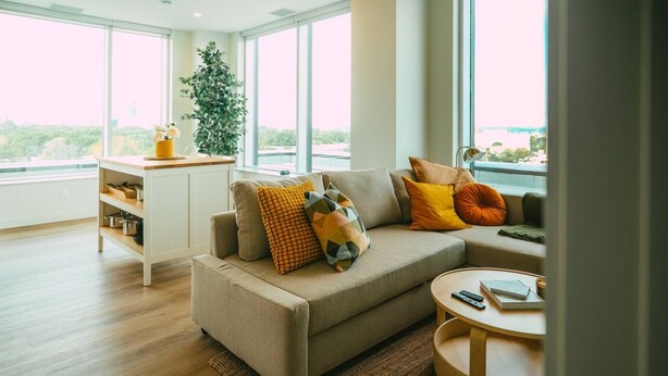 Een moderne woonkamer met een bank, een salontafel en een bijzettafeltje. Een groot raam biedt uitzicht op de omgeving.