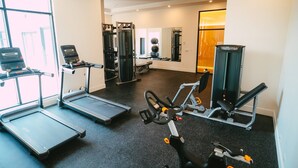 Un gimnasio con cintas de correr, una elíptica, una máquina de pesas y un espejo.