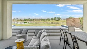 Un espacio al aire libre moderno con mobiliario y vistas a un campo de golf y una masa de agua.