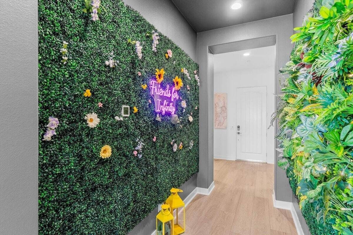 A hallway with a green wall covered in foliage and a neon sign that reads 'Friends for Infinity.'